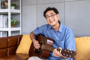 Happy man sitting on a couch playing guitar 快樂的男人坐在沙發上彈吉他 林口吉他課程